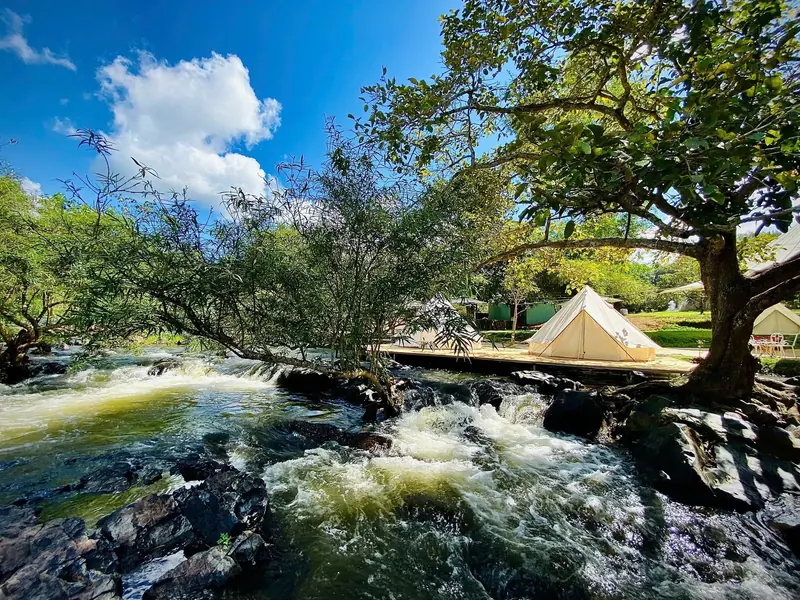 The stream flowing over rocky rapids under a blue sky, with white bell tents on a wooden deck on the bank